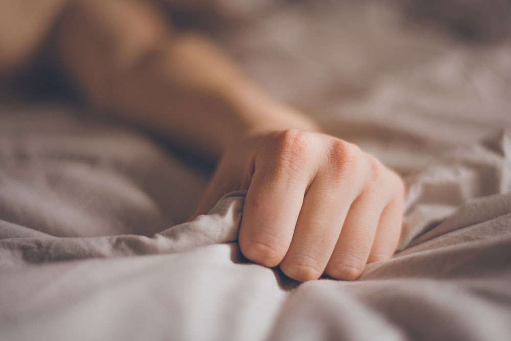 Hand einer Frau krallt sich in Bettdecke