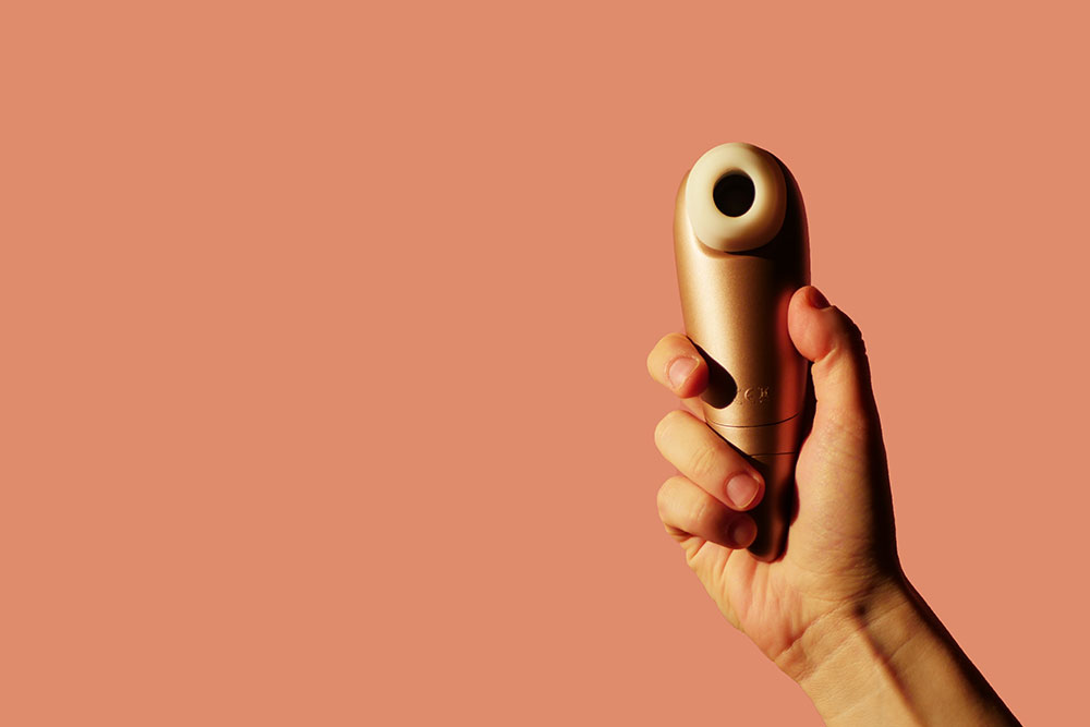 Hand hält Pulsator-Sextoy vor orangem Hintergrund