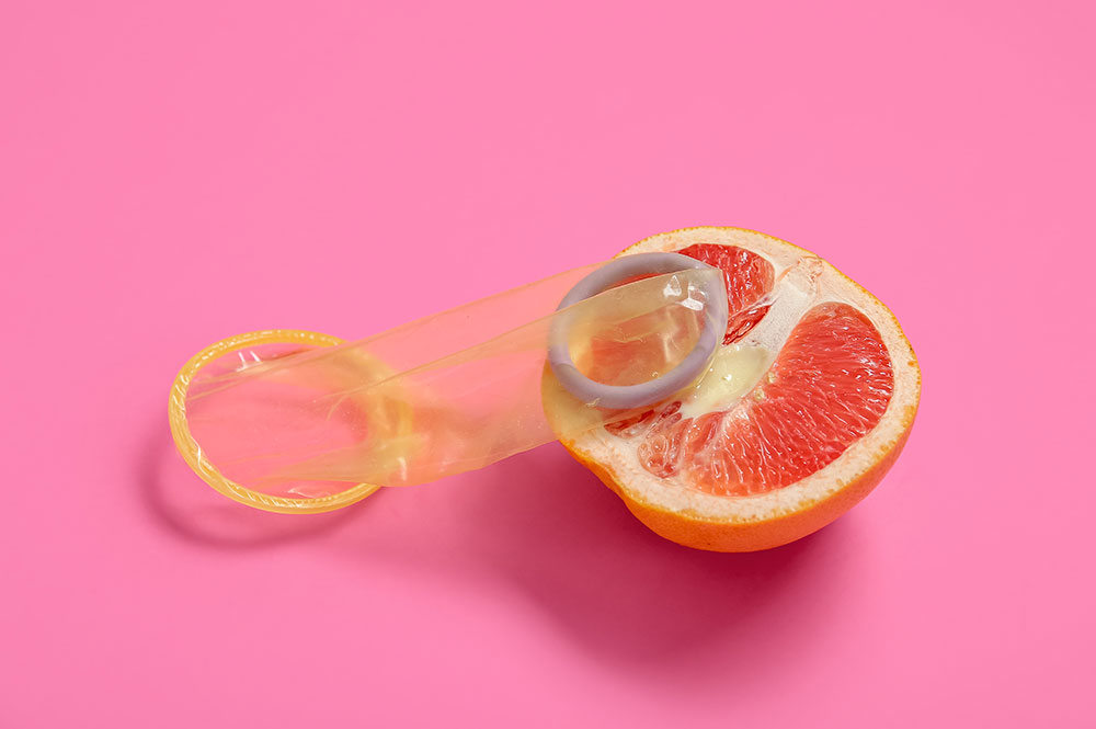 Aufgeschnittene Orange in Form einer Vulva, Femidom liegt darauf