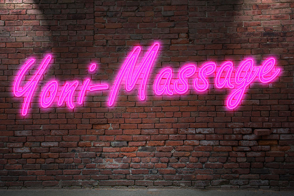 Rosa Leuchtreklame Yoni-Massage an Ziegelsteinmauer